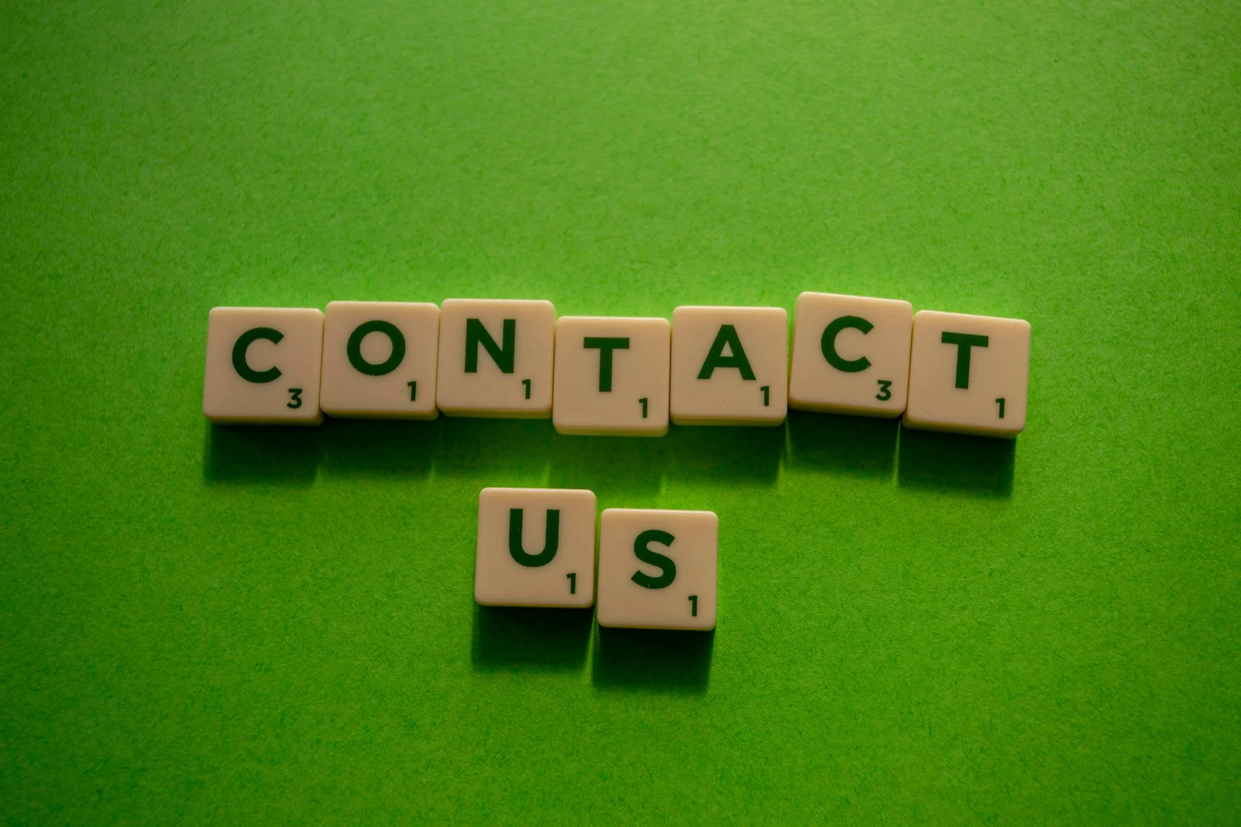 Scrabble tiles spelling 'CONTACT' and 'US' on a green background.