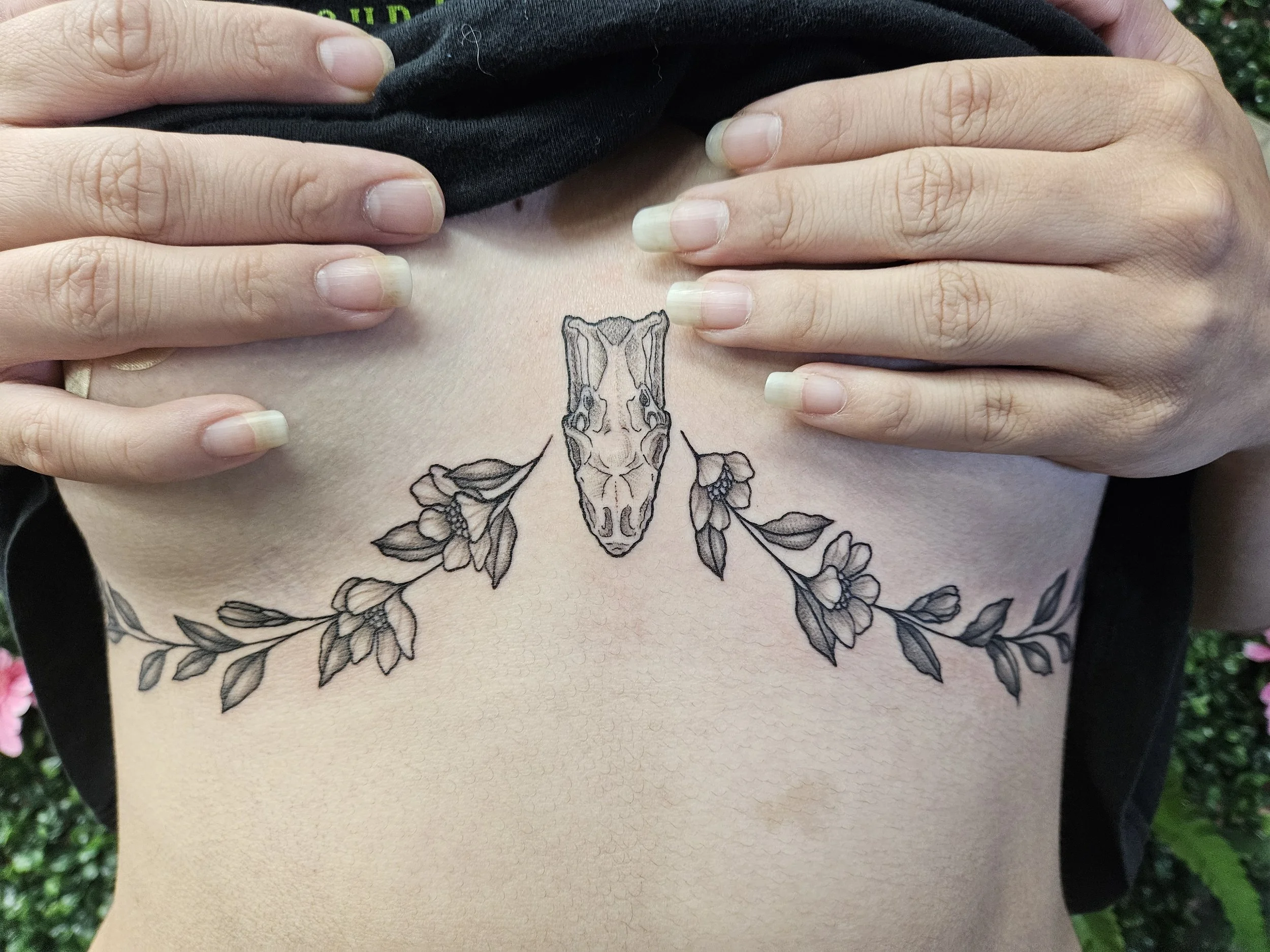 A tattoo on a person's lower chest and ribs showing a snake skull with floral and leaf motifs extending from both sides.