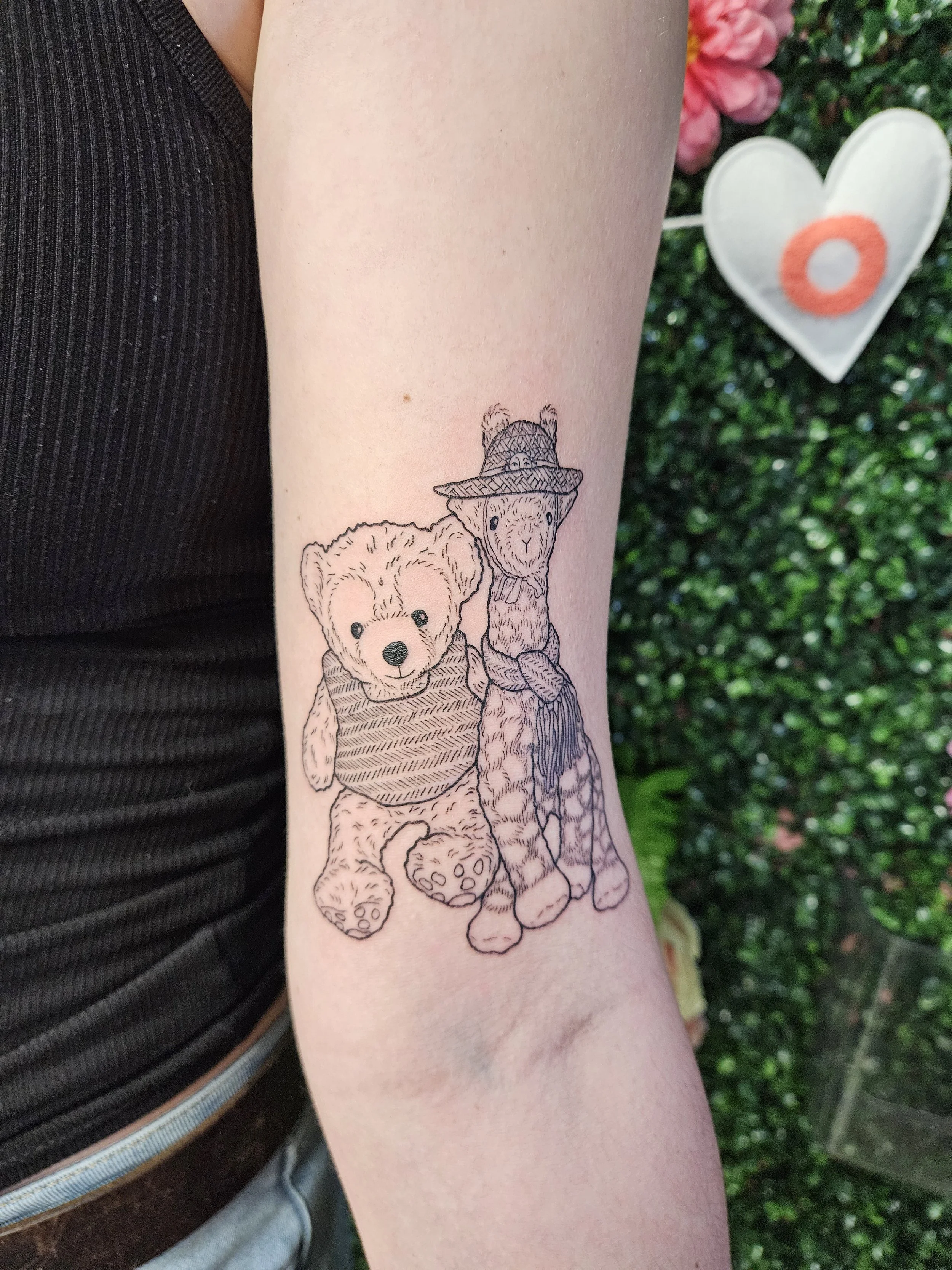 Tattoo of a teddy bear and a giraffe sitting next to each other on a person's forearm.