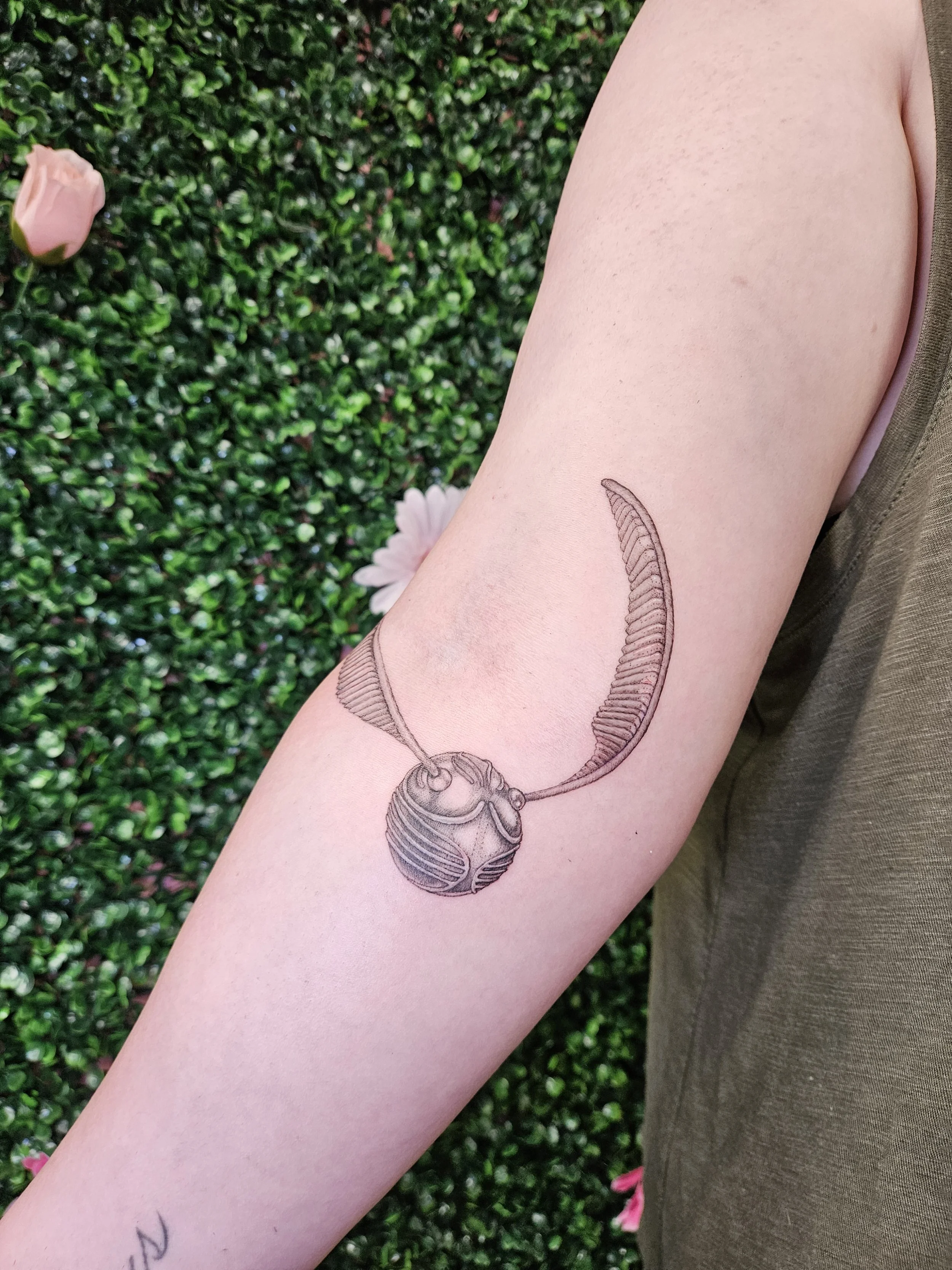 Tattoo of a Harry Potter Golden Snitch on a person's arm.