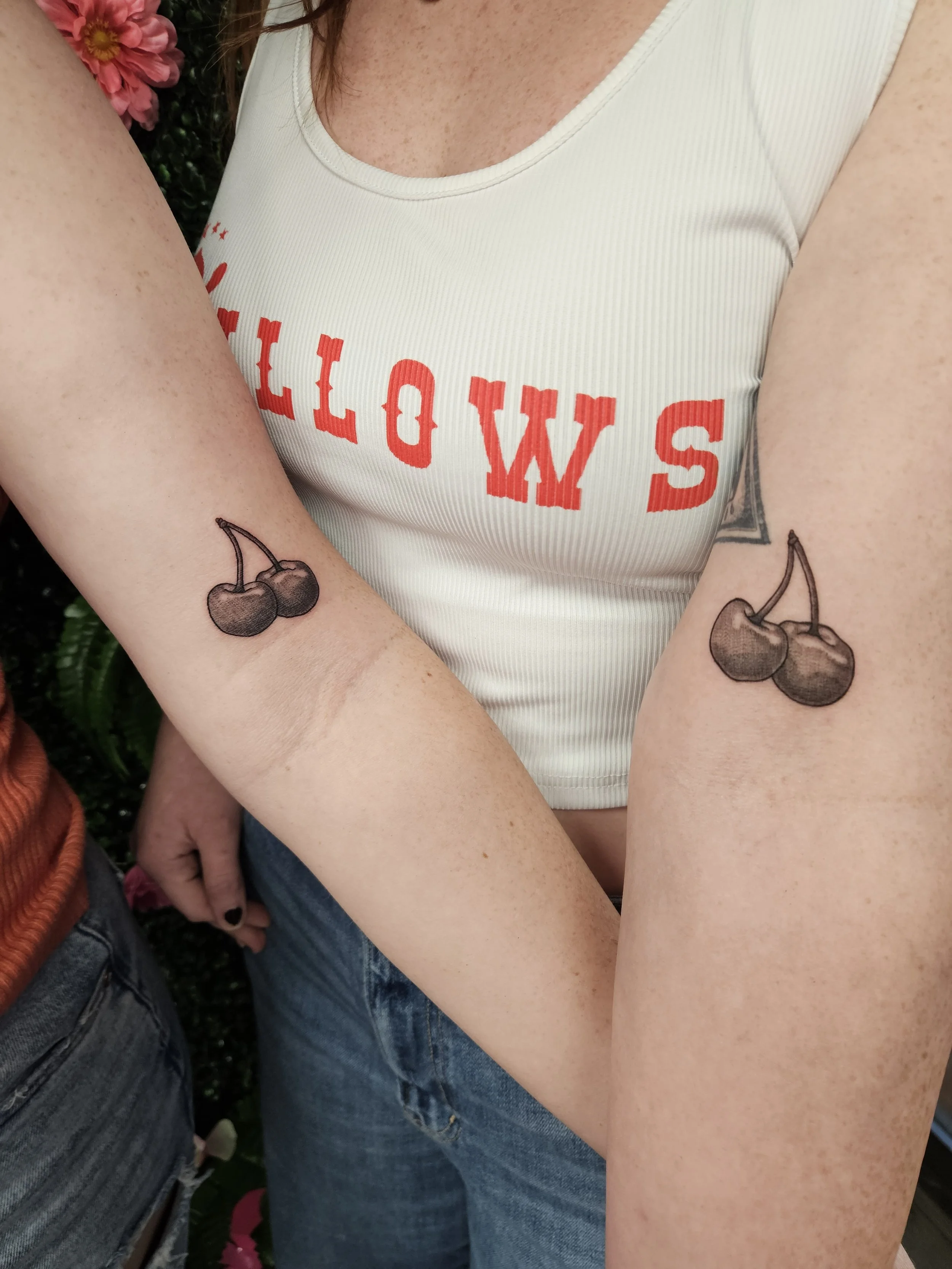 Two people showing matching cherry tattoos on their forearms.