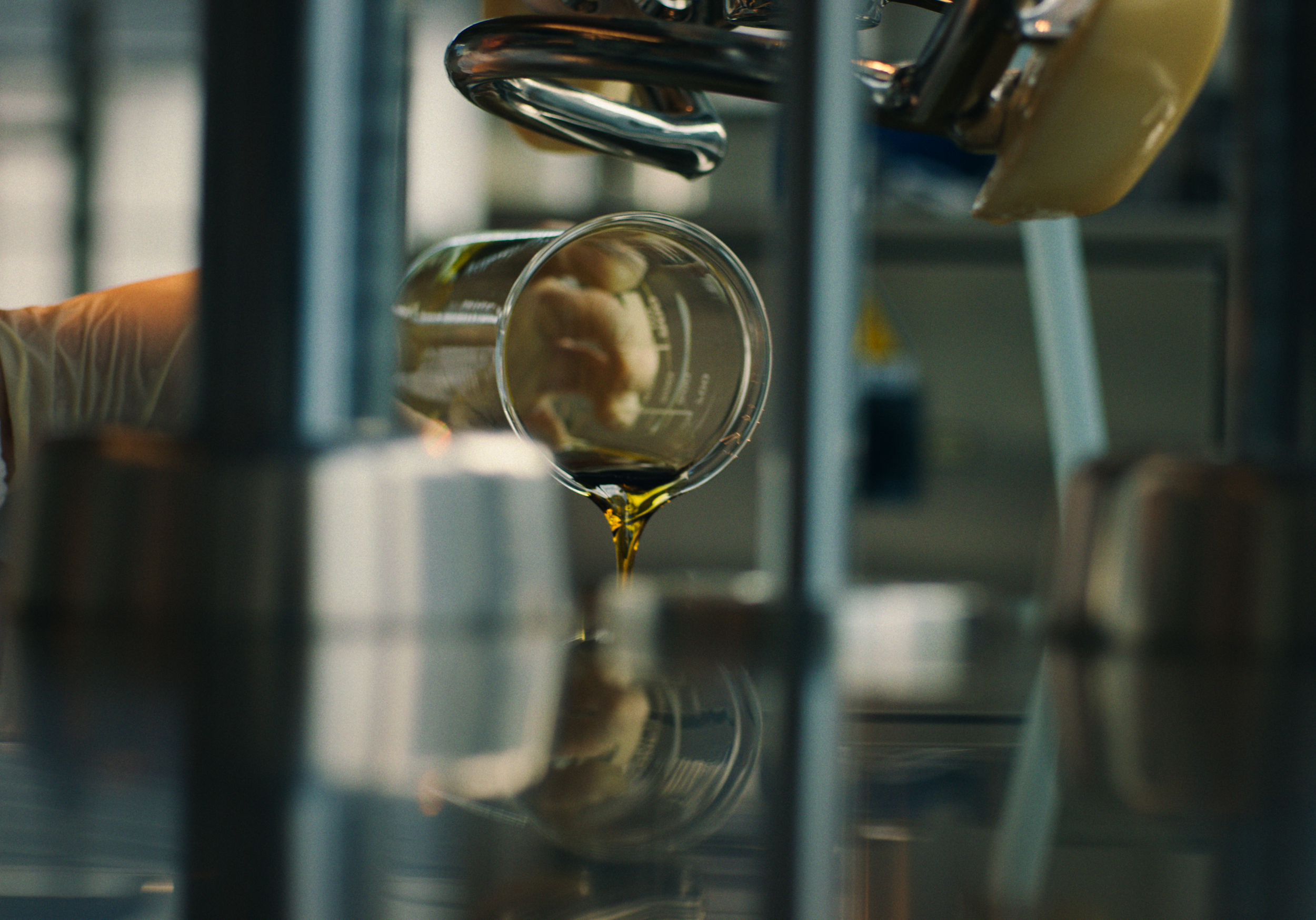 Liquid being poured into an overturned glass in a laboratory setting, surrounded by metal equipment and containers.