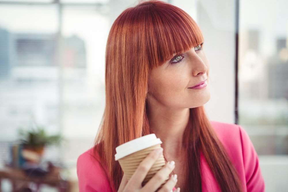 A woman with copper-toned hair looking at her reflection and touching her hair.