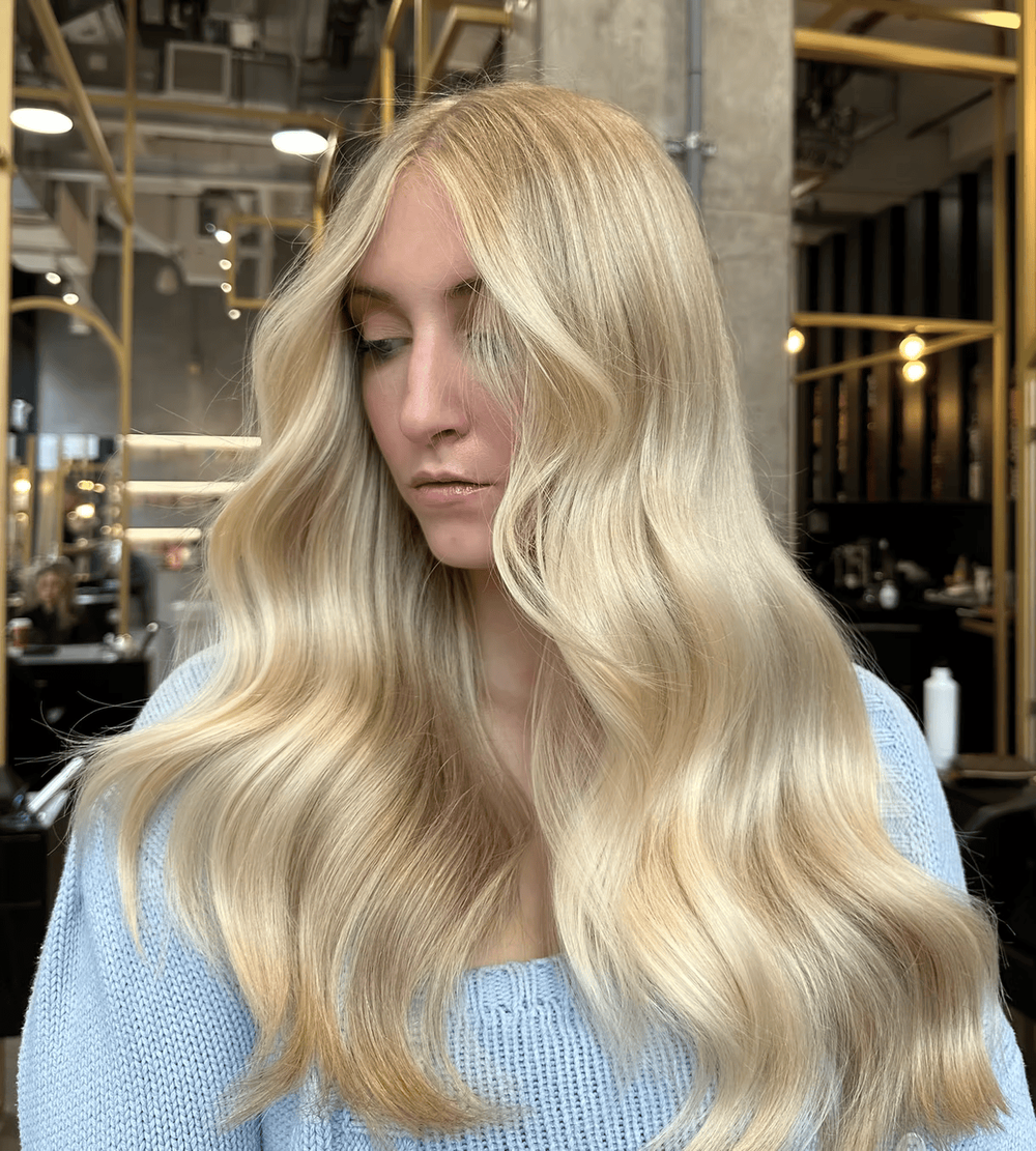 Balayage highlights weave through voluminous curls over a blue sweater