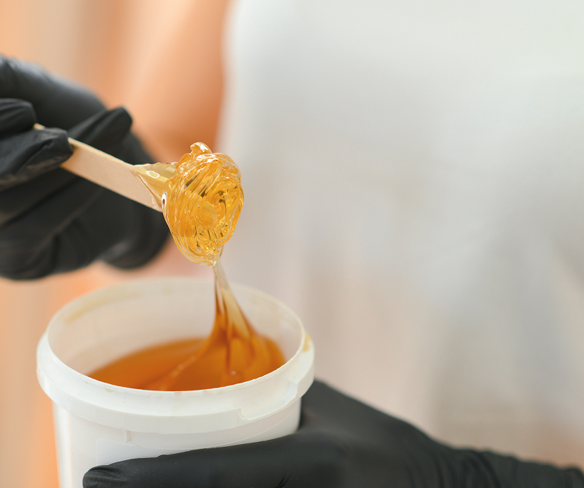 Body waxing Chicago esthetician in white applying golden wax to a client's leg with a spatula.