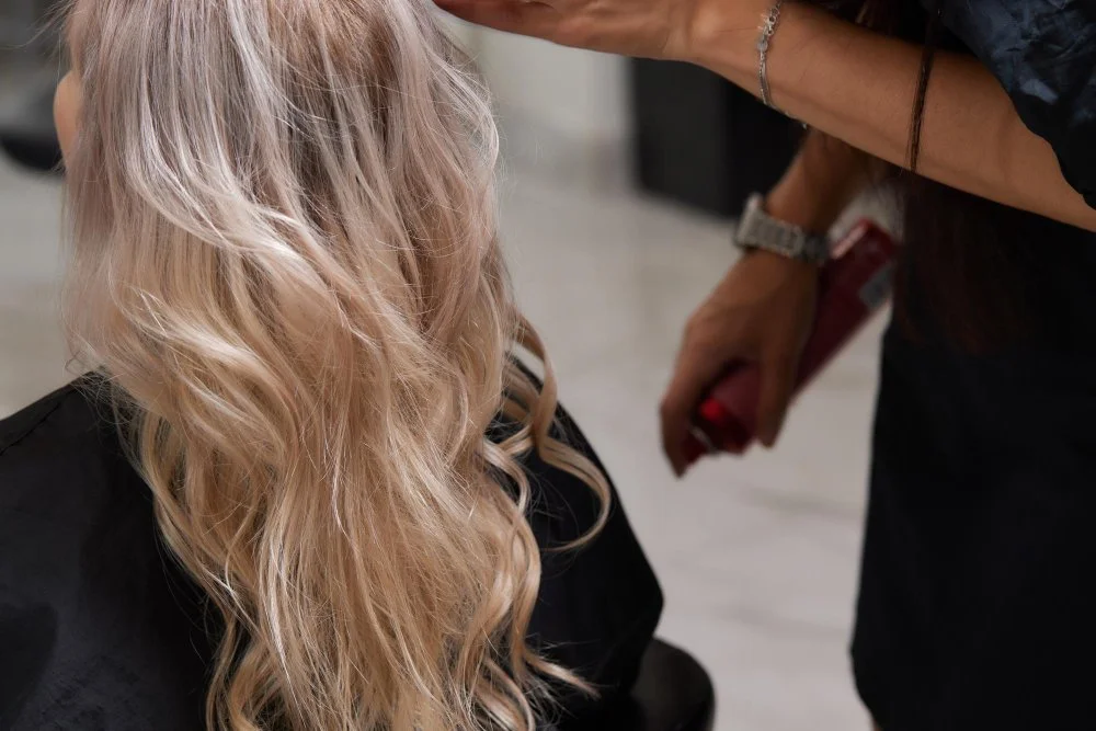 Stylist applying product to blonde balayage waves as part of a balayage maintenance routine.