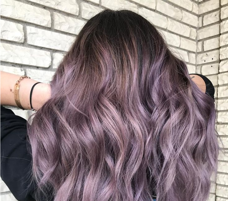 Best hair colorist in Chicago holding pink hair extensions beside a seated client in a salon.