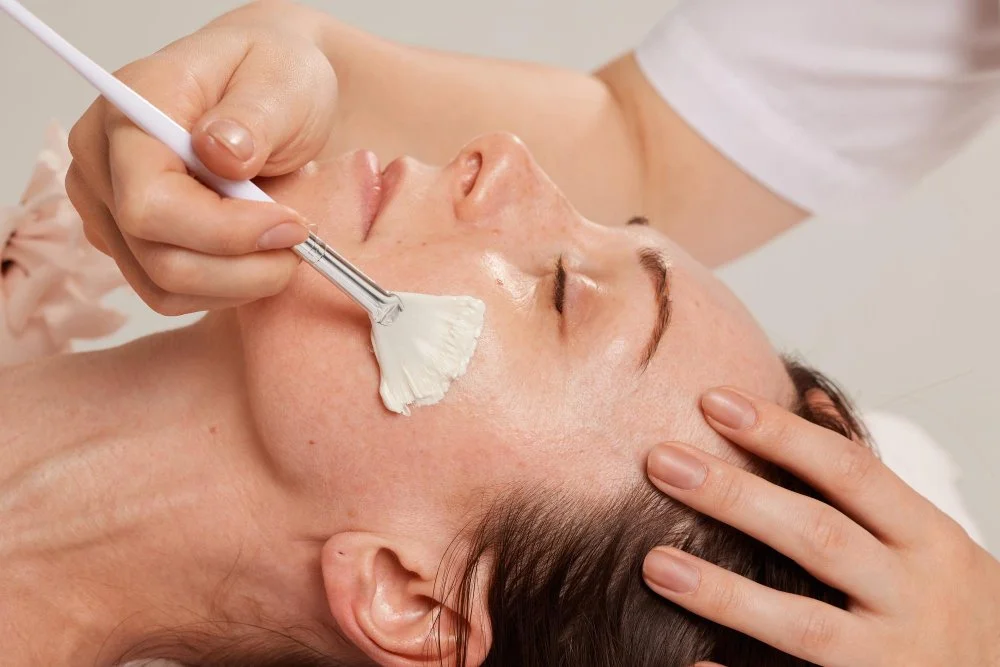 Professional applying exfoliating mask with brush on a woman’s face.