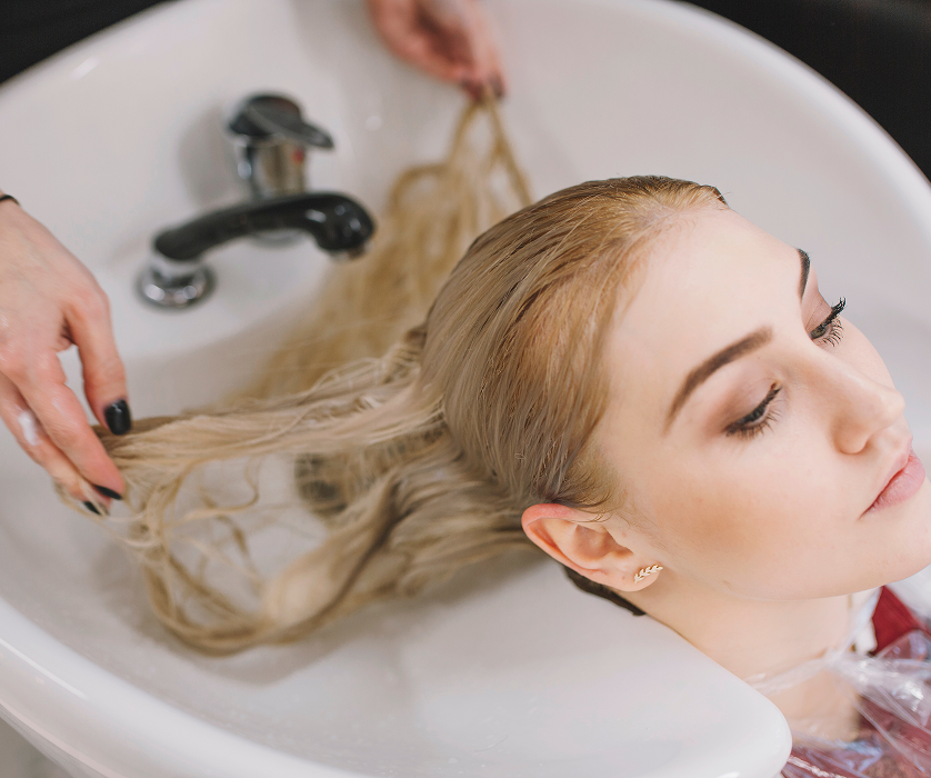 A professional stylist using a curling iron on a blonde client during a styling appointment at a hair salon.