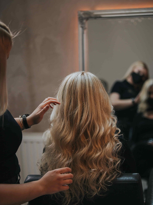 Stylist adjusts long blonde curls with soft face-framing highlights