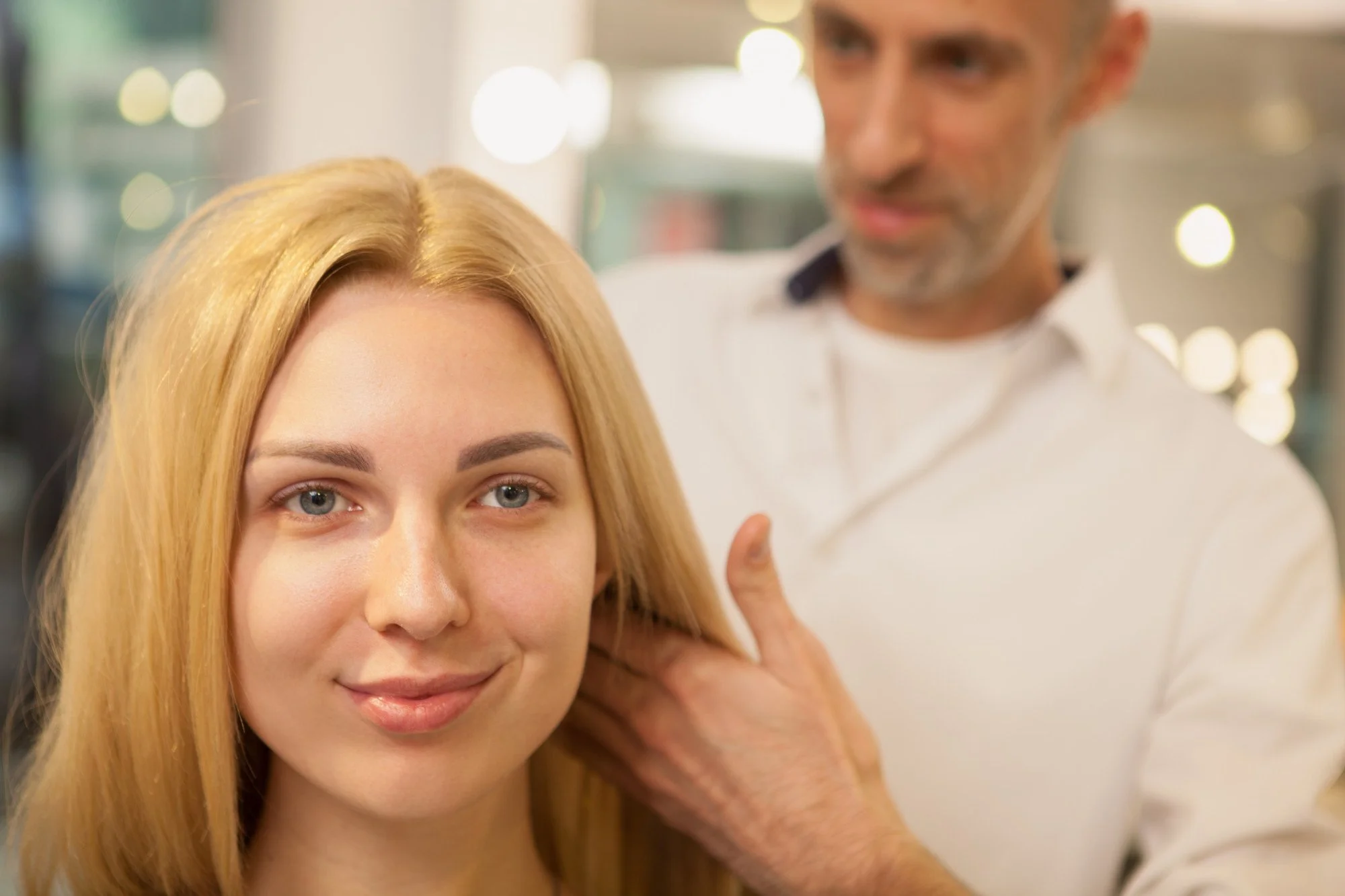 Young woman sitting in a salon chair while a hairdresser styles her long hair.