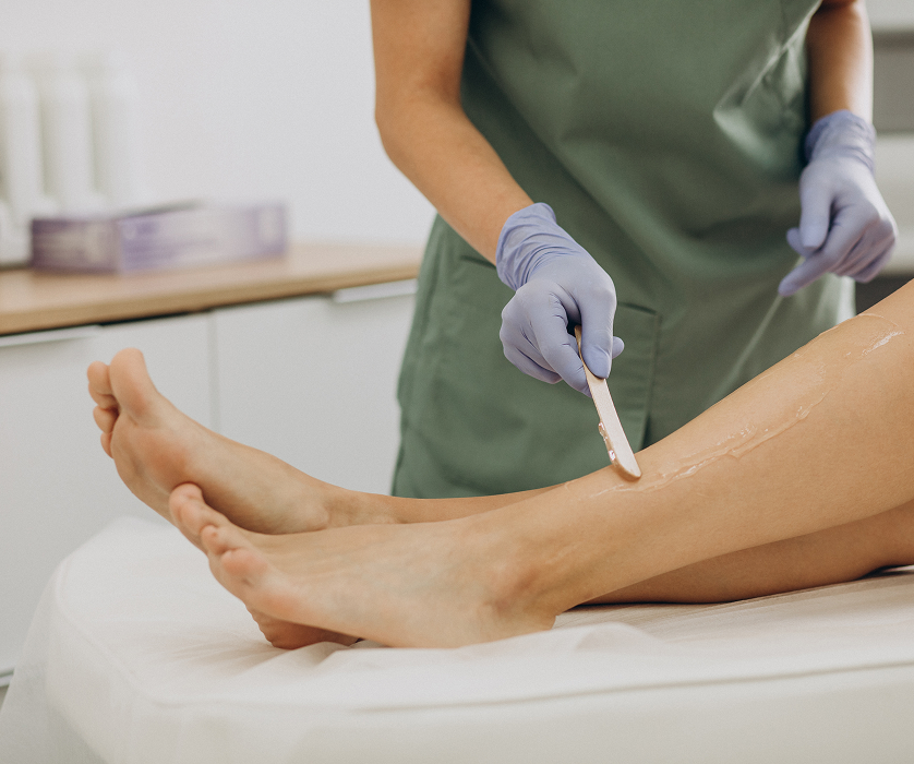 Sugar waxing in Chicago, of honey-toned wax being applied to a client's knee with a spatula.