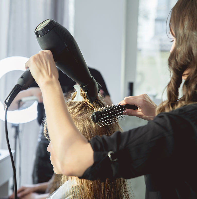 Stylist using a round brush and dryer to smooth and shape hair during a professional blowout service.