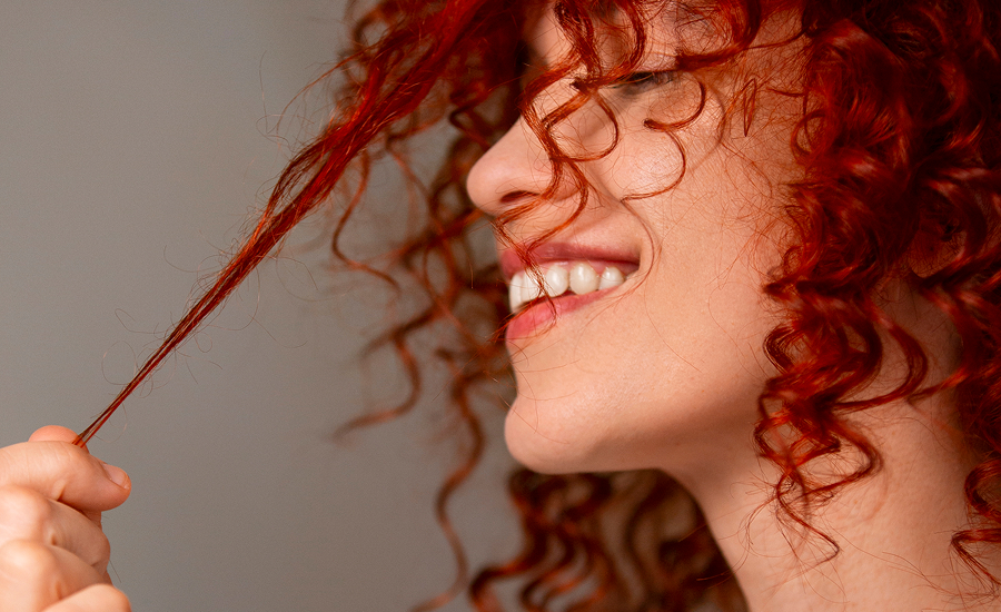 "Young woman with curly dyed hair smiling, showcasing vibrant color and how to make hair dye fade faster"