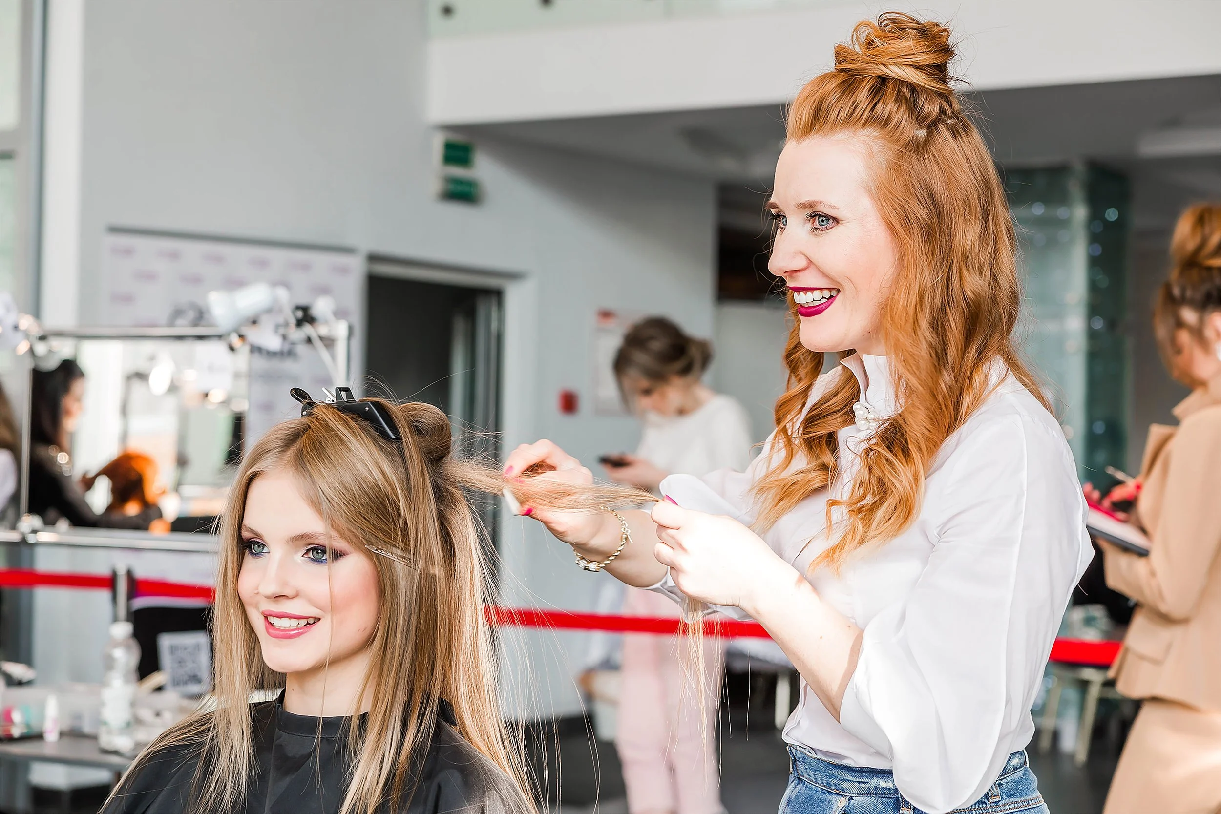 A redheaded stylist styling a blonde client's hair at a women's hair salon.