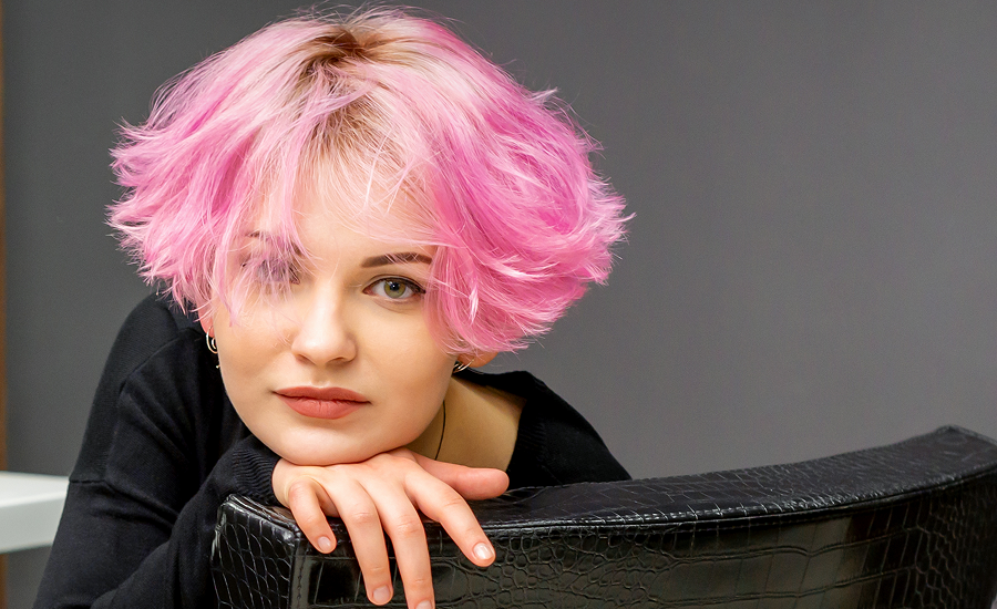 A woman with a fresh, short pink hairstyle sits in a beauty salon chair, showcasing a bold style inspired by 2025 hair color trends.