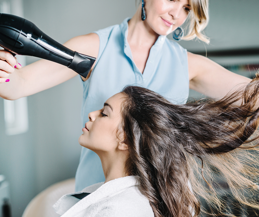 Salon stylist lifting and drying long hair to create volume and movement in polished blowout hair.