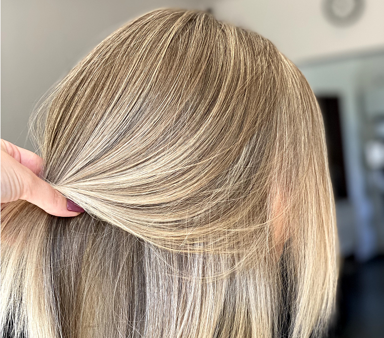 Long hair mid-process during a freehand lightening technique, showing hand-painted application from behind at a hair color salon.
