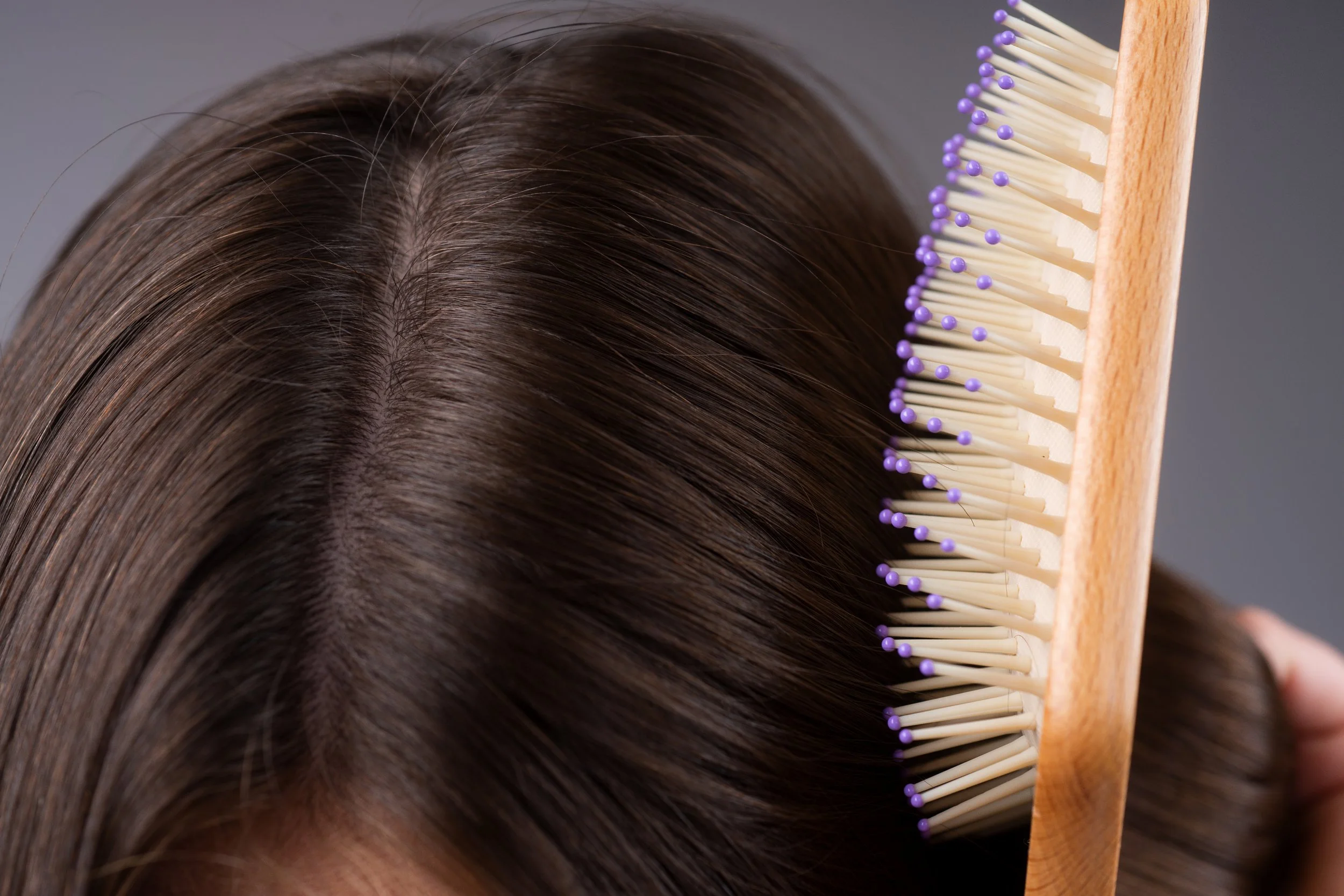 A woman brushing her scalp with a wooden brush shows a common cause of scalp flaking.