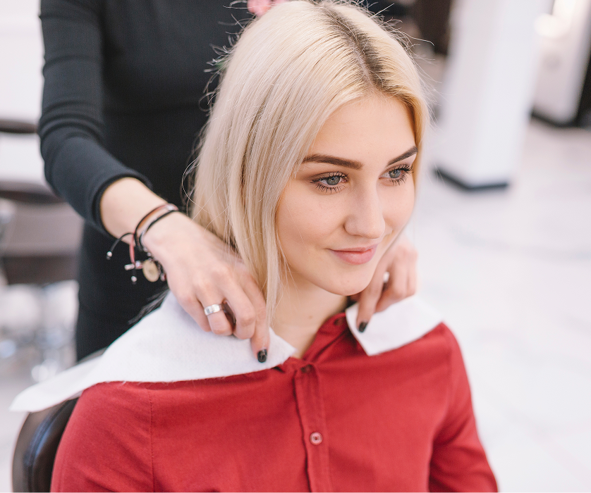 A hairdresser styling a young woman's hair during a salon appointment.