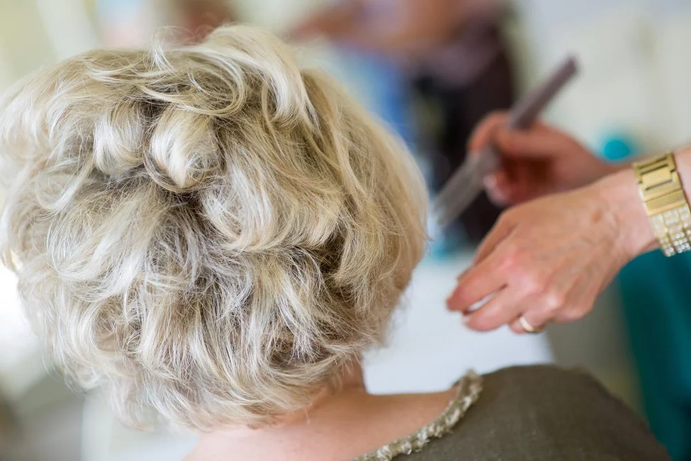 A stylist shaping a woman's short platinum cut in a salon, showing hair color ideas to look younger for women over 60.
