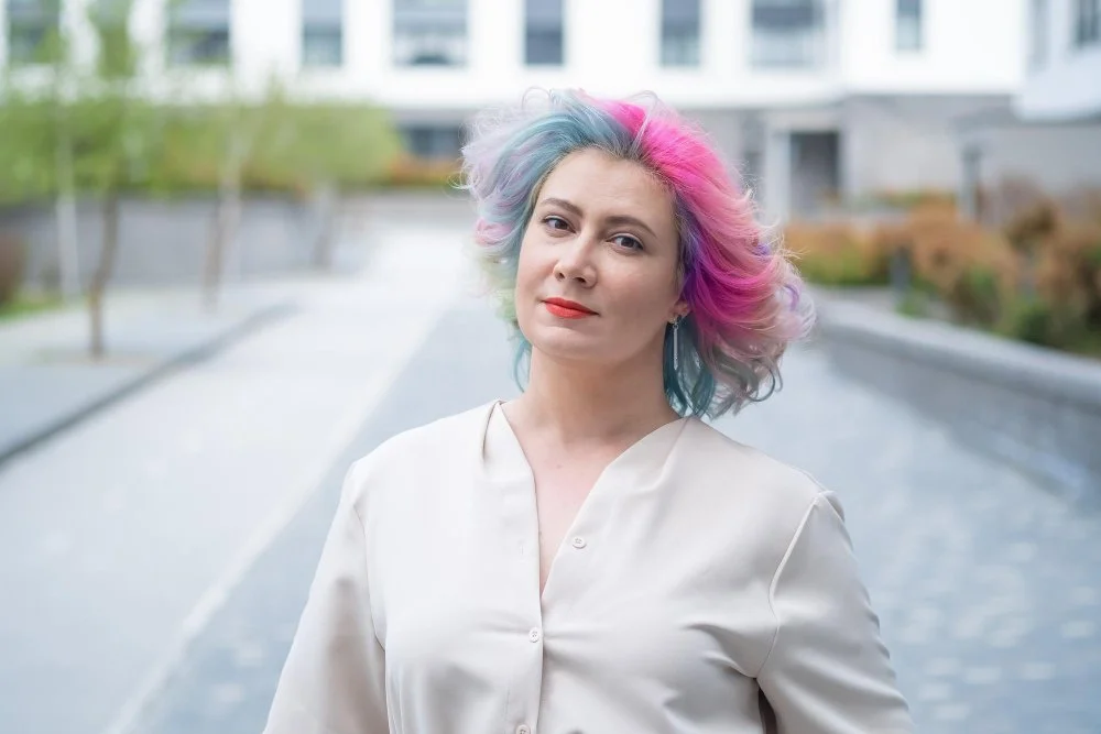 A woman with vibrant pastel rainbow hair standing outdoors, showing bold hair color for women over 60.