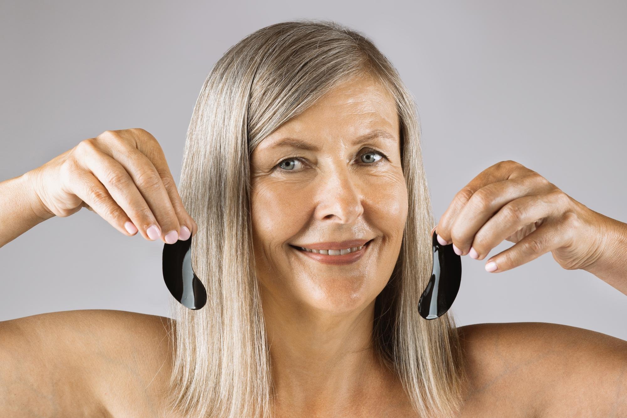 A smiling woman compares lighter and darker gray-blended shades to explore what color hair makes you look younger