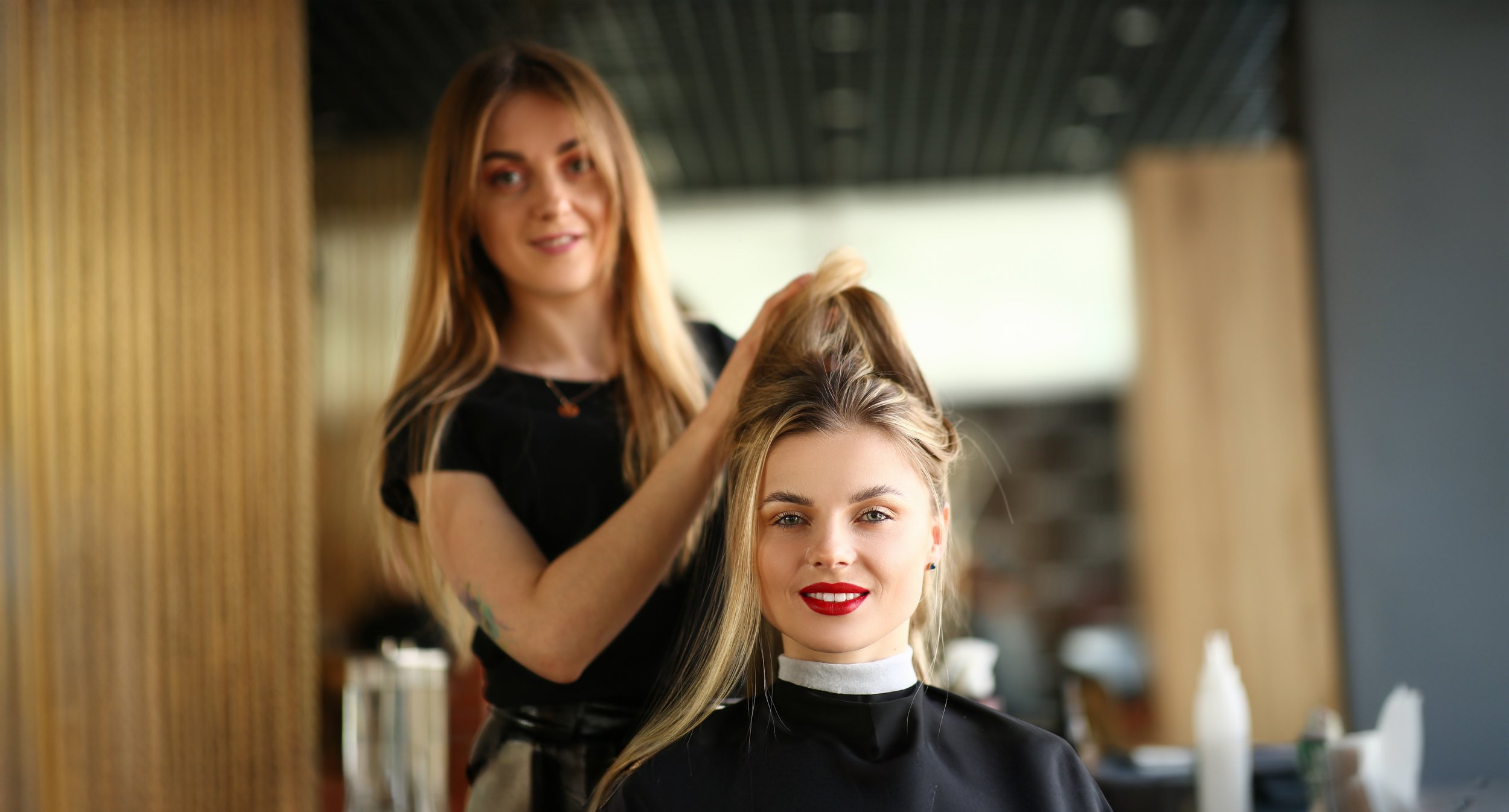 A stylist brushing a client's long blonde hair while she smiles in a salon chair.