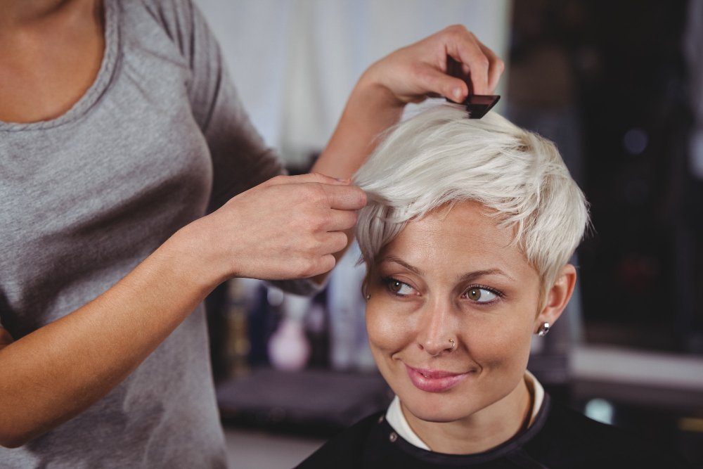 A stylist shaping a woman's short platinum cut in a salon, showing hair color ideas to look younger for women over 60.