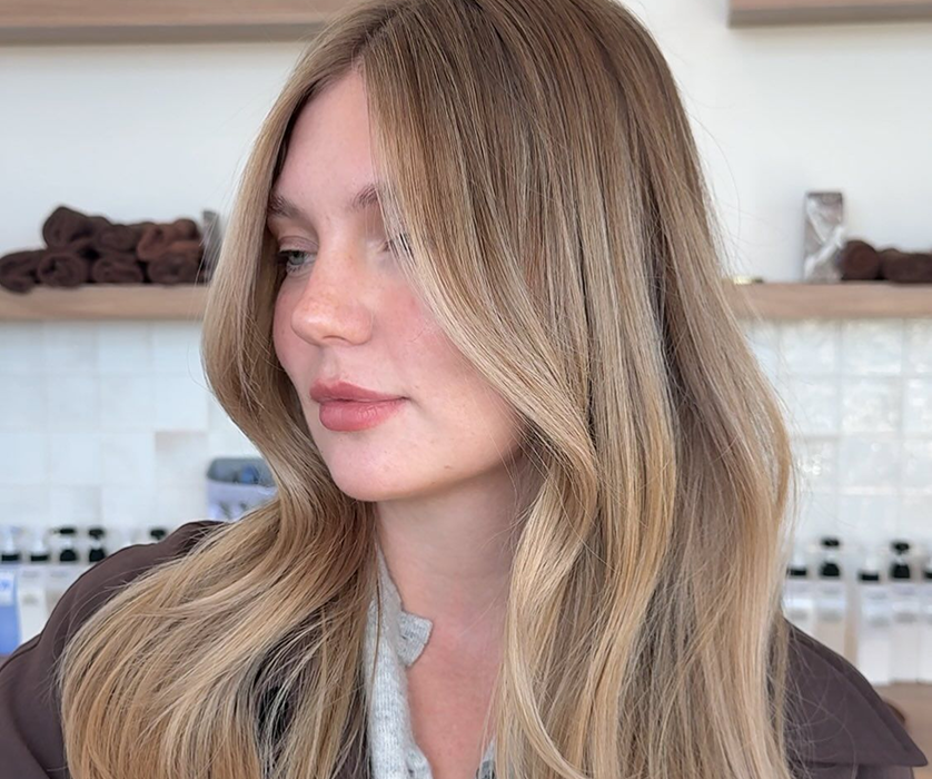 A Chicago hair colorist smiling while sectioning a client's dark hair with a brush.