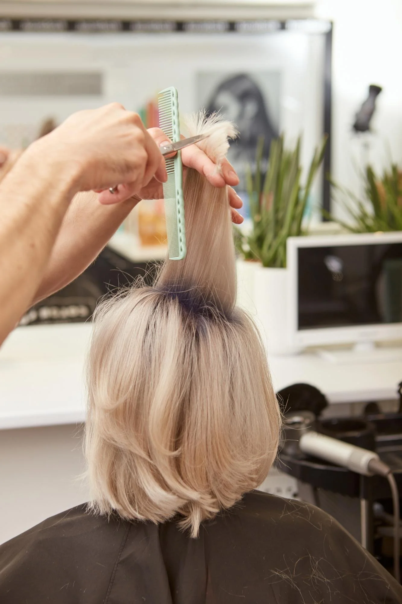 A hairdresser cuts the blonde hair of a woman in a beauty salon, performing maintenance for color-treated hairstyles.