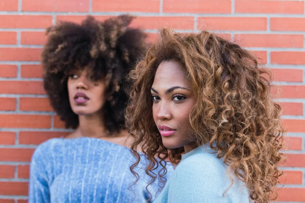 Two women with textured curls showcasing diverse natural hair colors in a realistic, everyday look