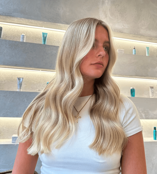 Blonde balayage waves flow past the shoulders in a sunlit salon