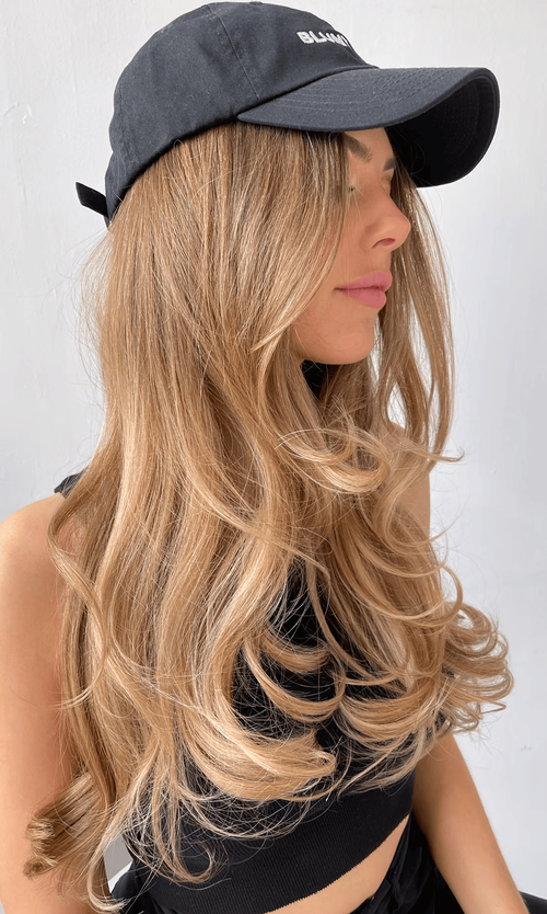 Long layered waves fall past the shoulders in warm honey-blonde tones