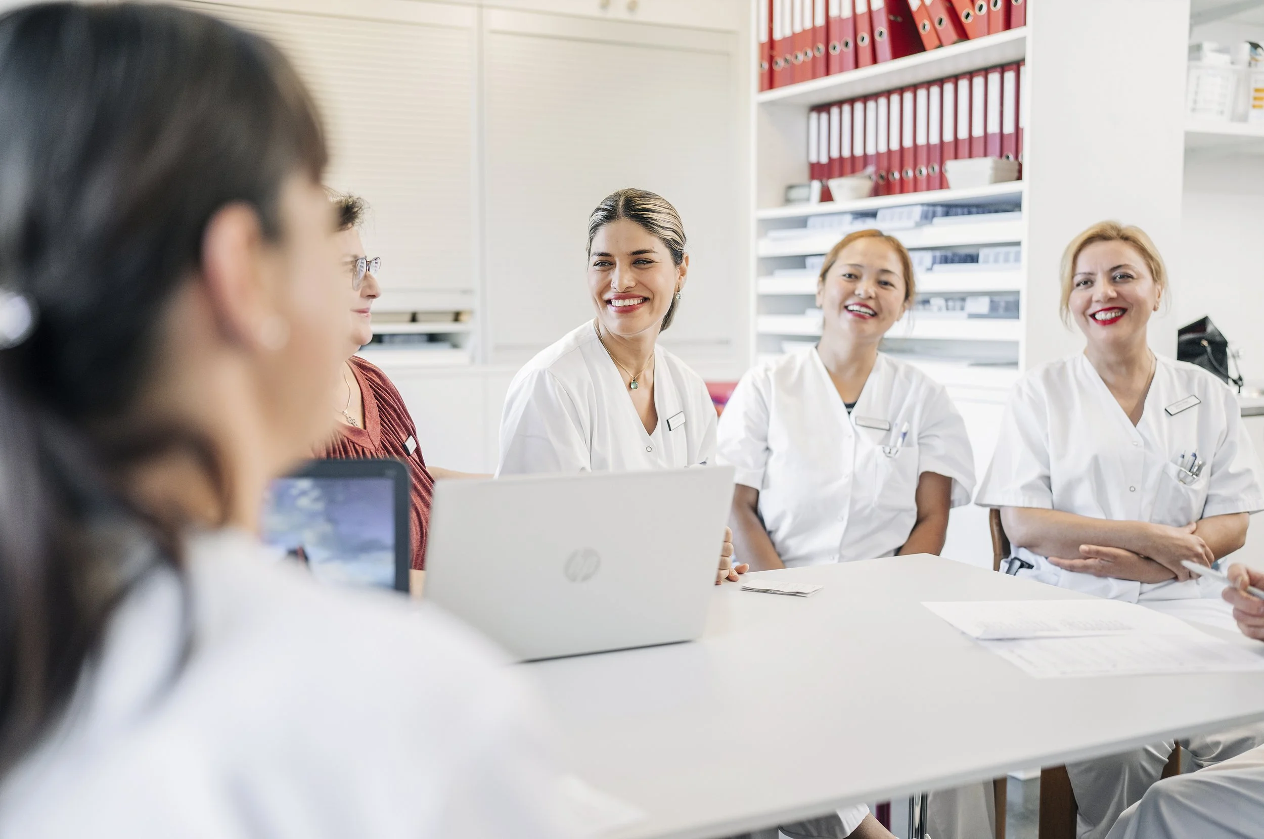 Gruppen von medizinischen Fachkräften, die bei einem Meeting im Krankenhaus arbeiten, alle tragen weiße Kittel und sitzen an einem Tisch.