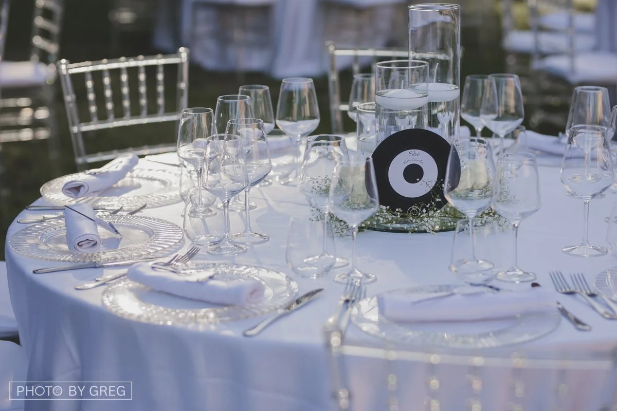 Tavola elegante, centrotavola floreale con specchi e vetri con candele, tema musica con disco vinile. Tovaglioli bianchi con stellina luminosa per il taglio torta
