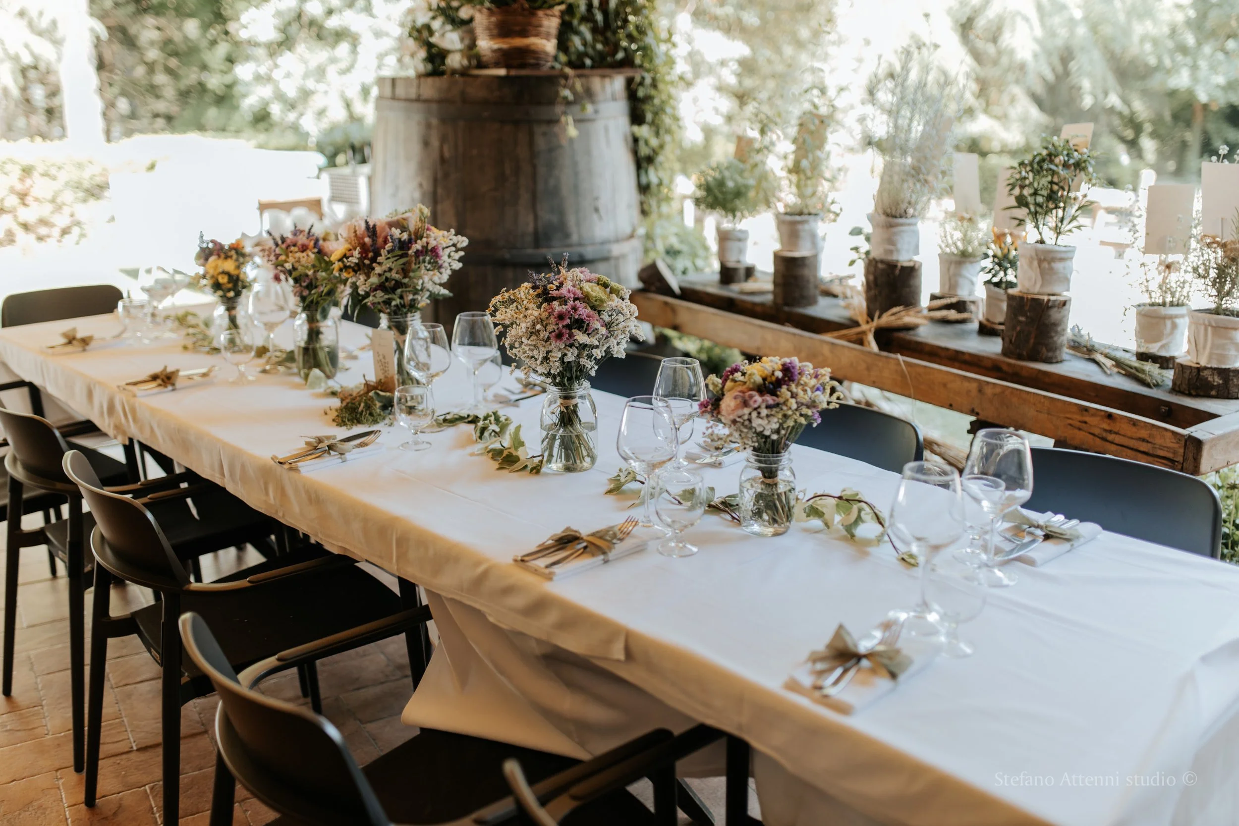 Tavola lunga per il ricevimento di matrimonio, con composizioni floreali e dettagli coordinati sotto una struttura in legno. Matrimonio rustico su tavolo imperiale