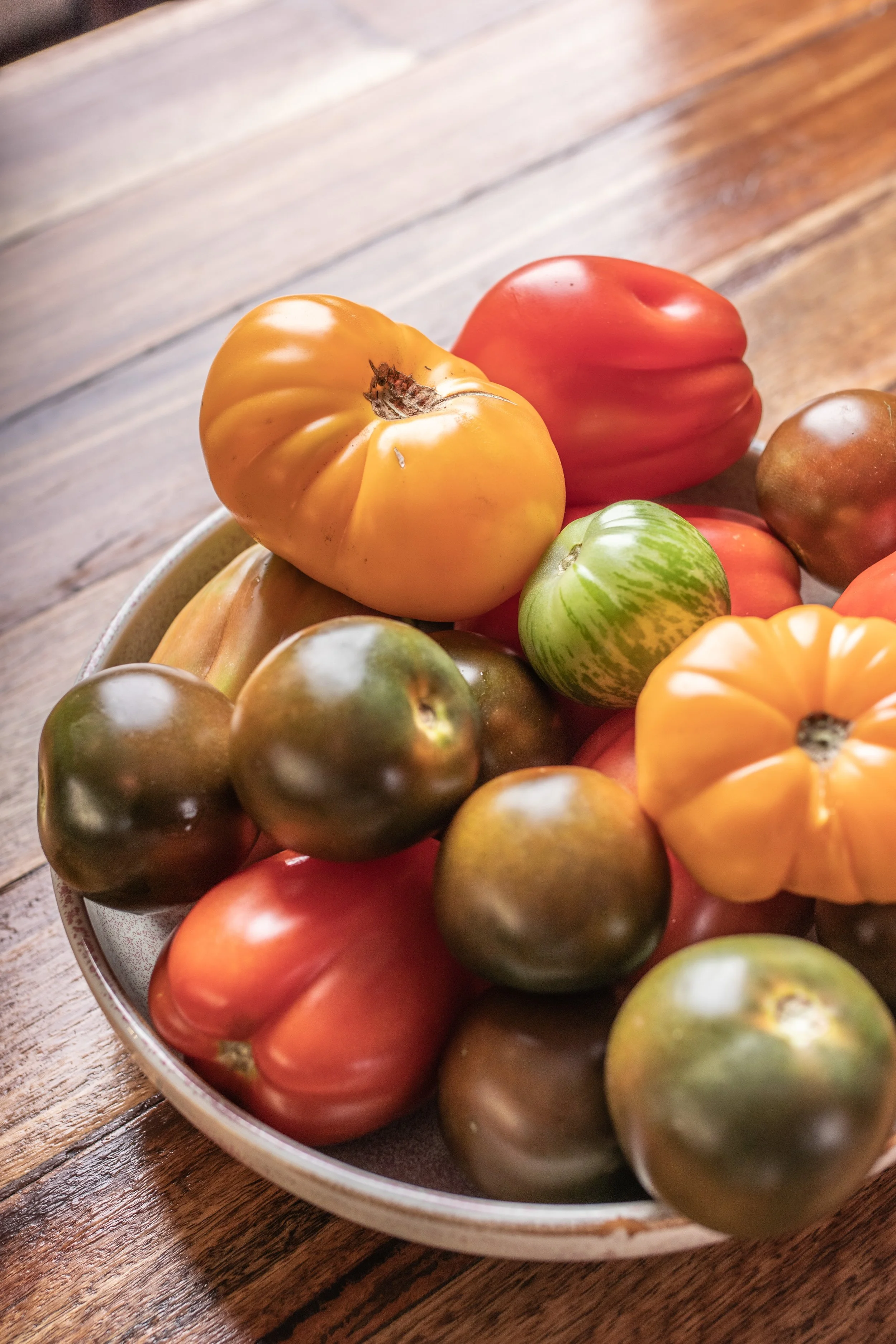 A bowl of heirloom tomatoes on a wooden table.
