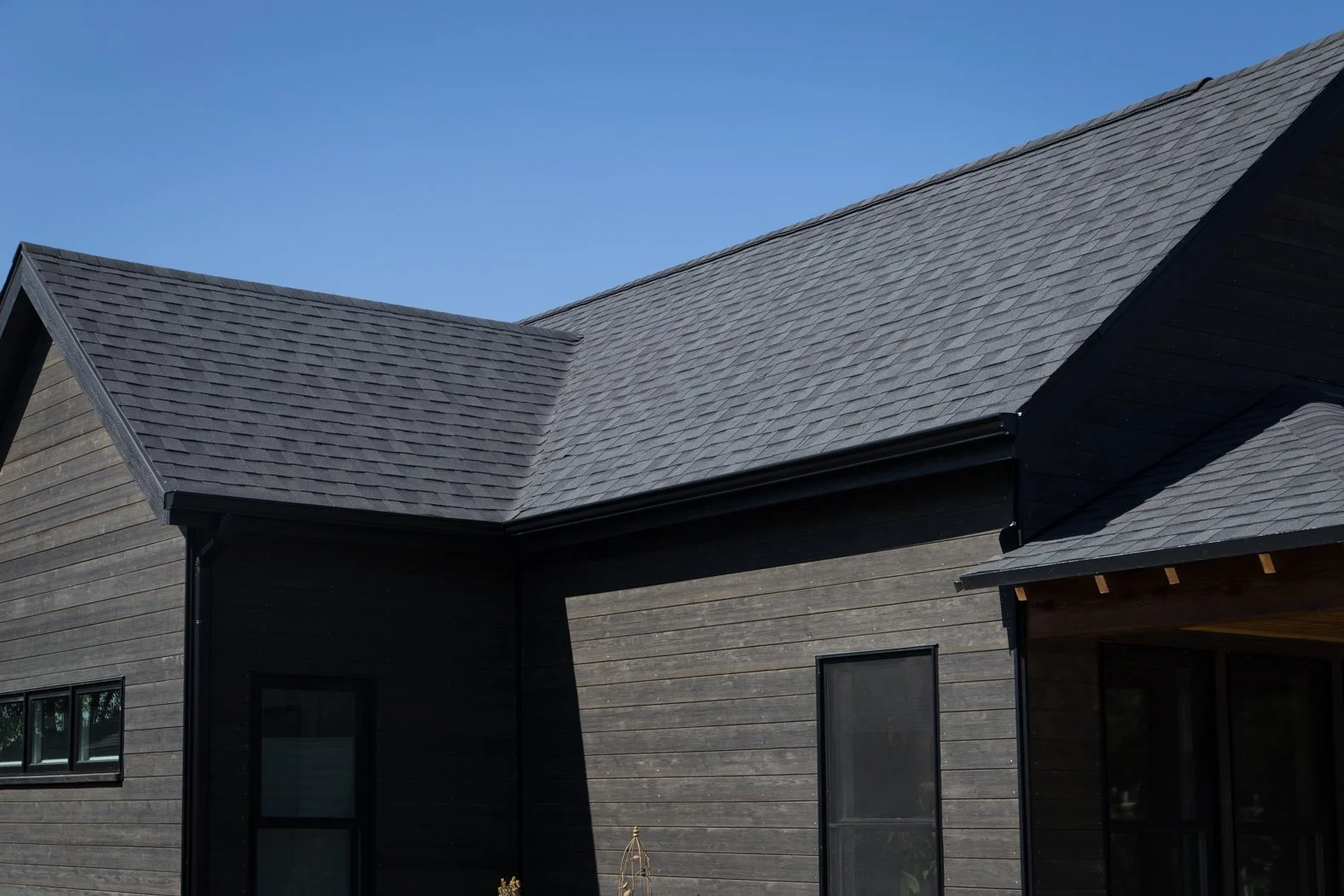 A black wooden house with a sloped roof and black window frames under a clear blue sky. Roofing Company in Denver Colorado