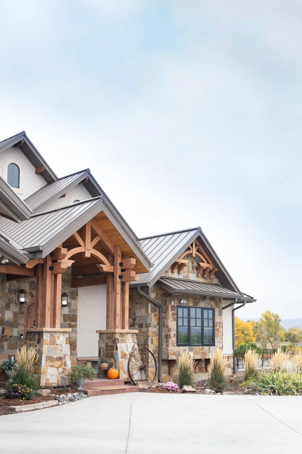 Exterior of a house with stone facade, wooden accents, metal roof, and landscaped yard with pumpkins and flowers. Roofing Company in Denver Colorado