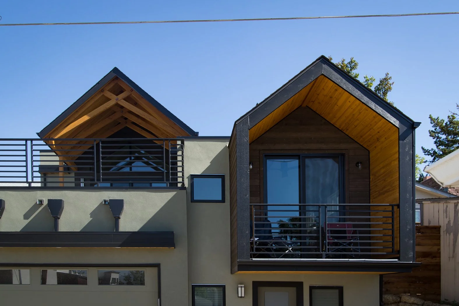 Modern house with two small gable roofs, a balcony with black metal railing, and large glass doors, under a clear blue sky. Roofing Company in Denver Colorado