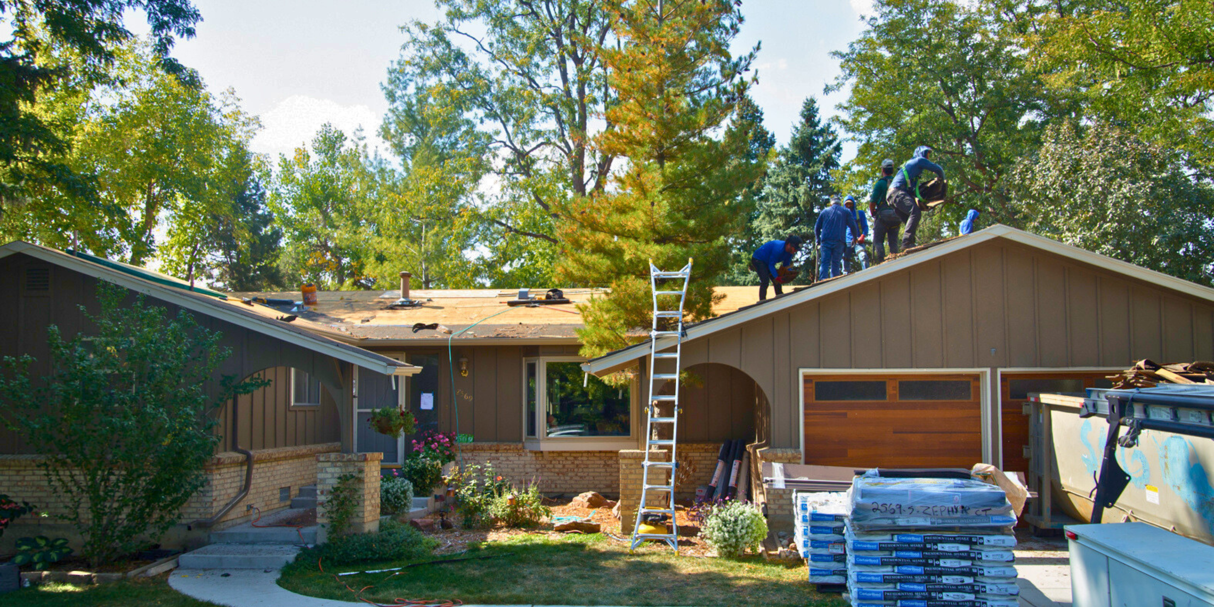 Construction workers on the roof of a house replacing or repairing shingles, with debris, tools, and building materials nearby. Roofing Company in Denver Colorado