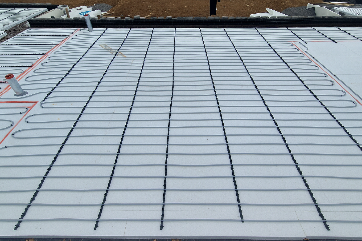 Underfloor heating installation on a flat roof, with white panels and black heating pipes arranged in parallel lines.