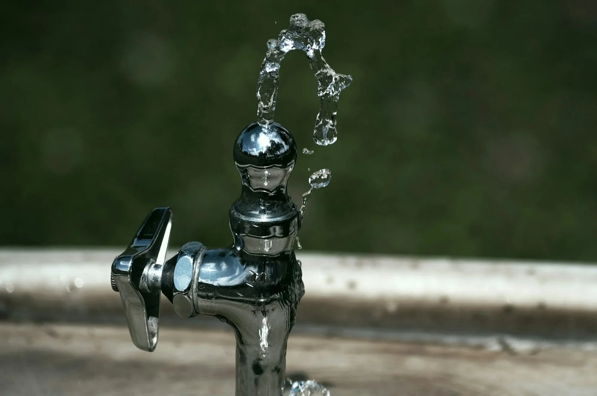 A close-up of a metal outdoor faucet with water splashing out.