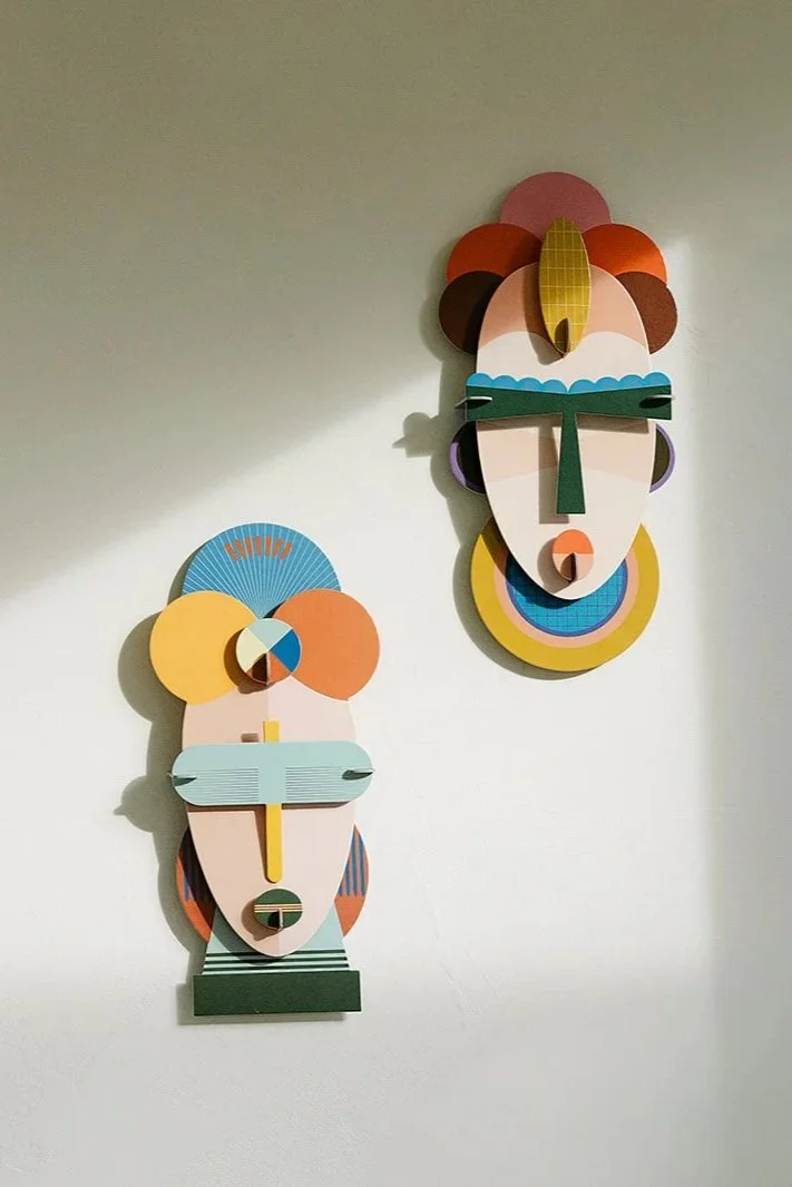 Twee abstracte kunstwerken van gezichten gemaakt van gekleurde, geometrische vormen, hangen aan een witte muur.