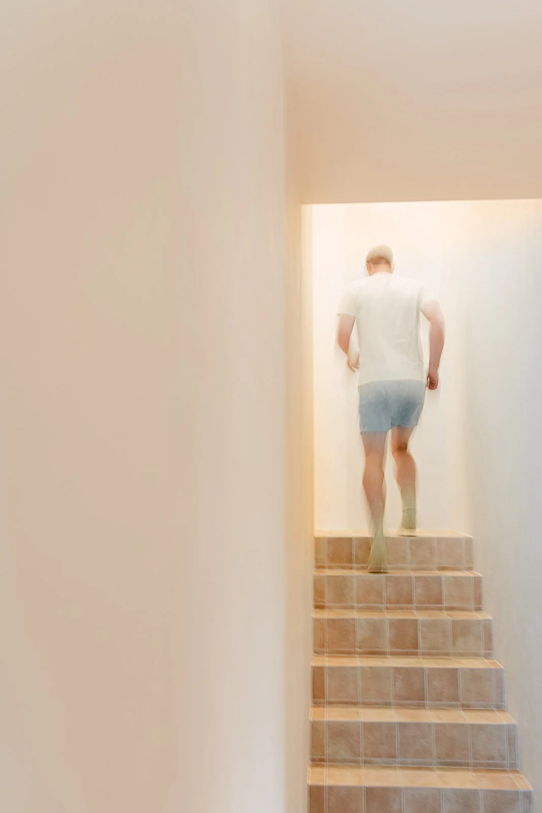 Man die de trap oploopt vanuit een lichte, minimalistische muur, gekleed in een wit shirt en denim shorts.