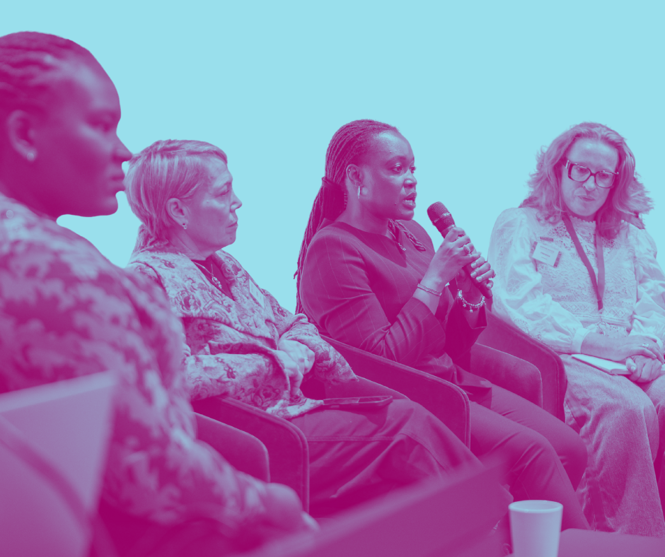 Women sitting in a panel discussion, with the woman in the center holding a microphone and speaking.