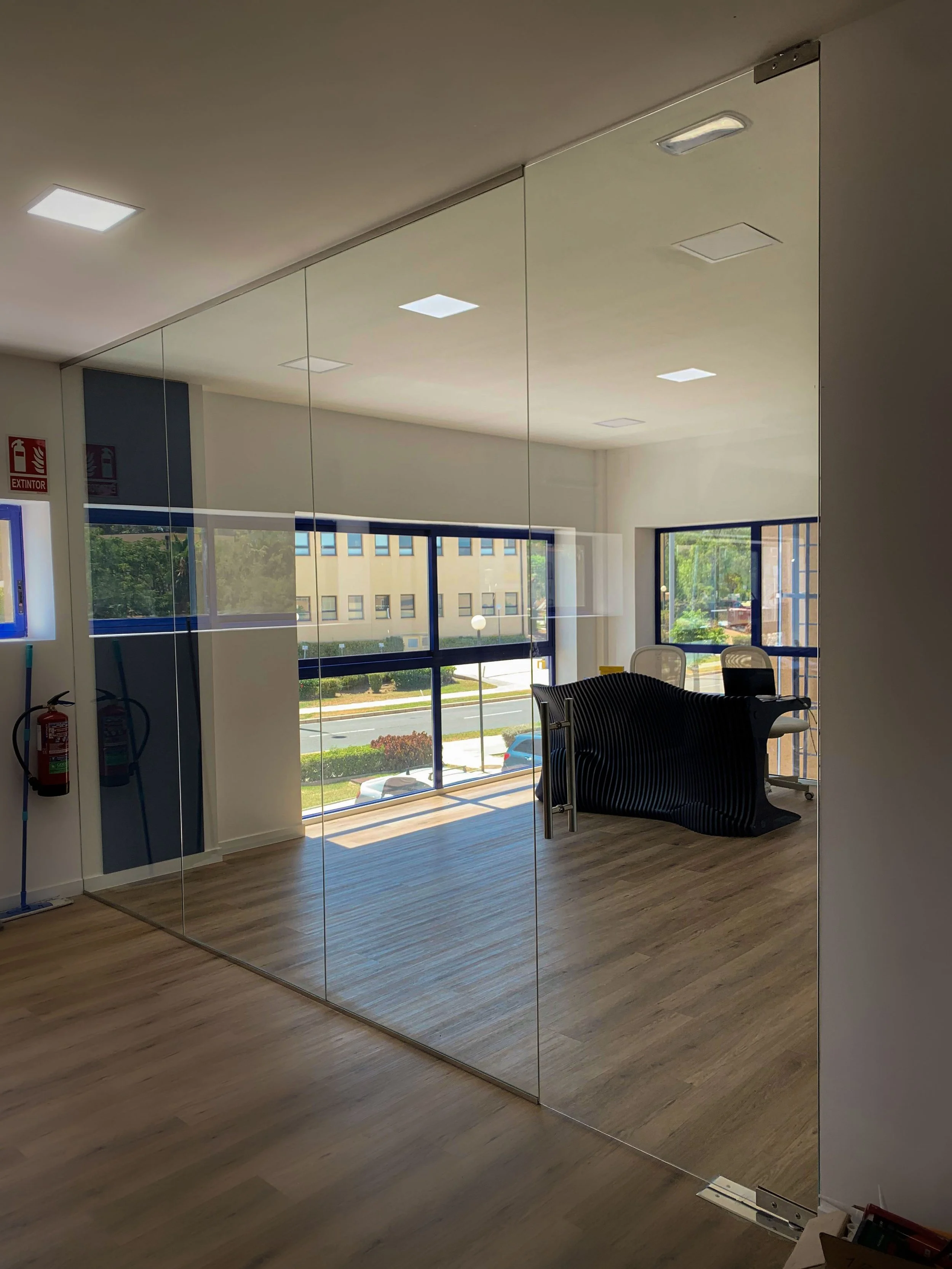 Muro de vidrio con sujeciones de acero y puerta con pernio hidráulico.