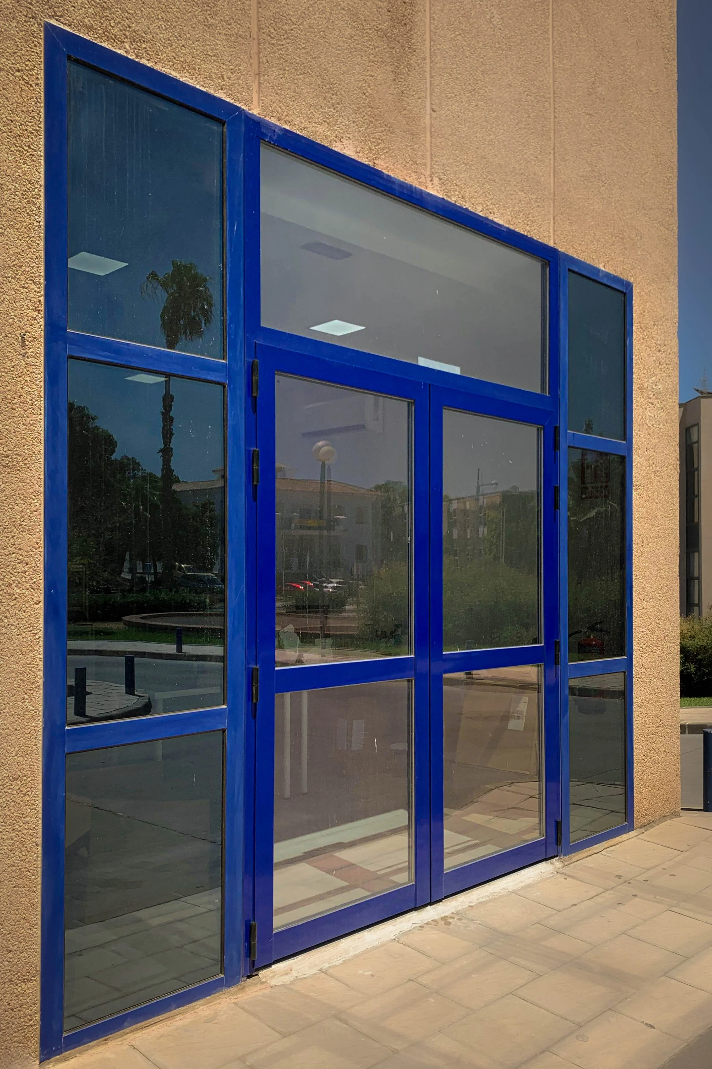 Puerta de aluminio azul con cristales fijos tipo Climalit para aislamiento térmico. Barra antipánico para salida de emergencia.