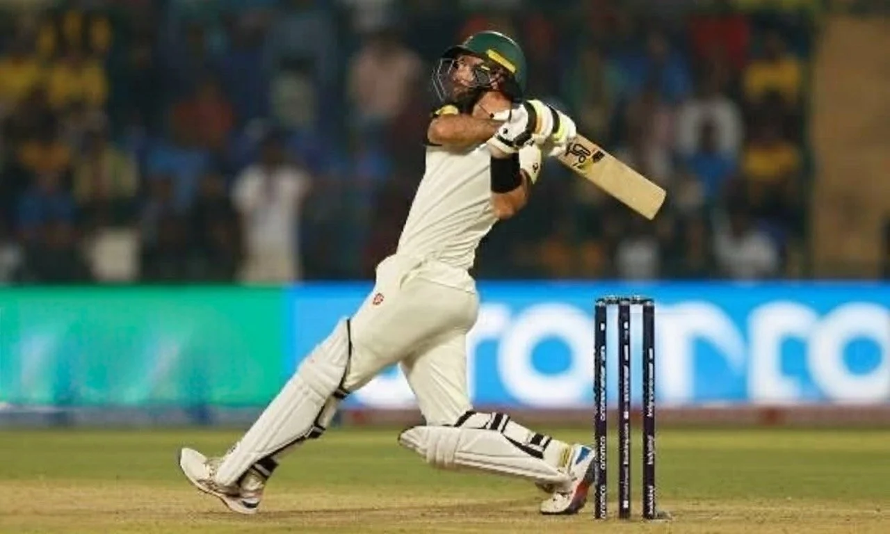 Cricket player wearing white uniform, helmet, and gloves, hitting a cricket ball with a bat on the field.